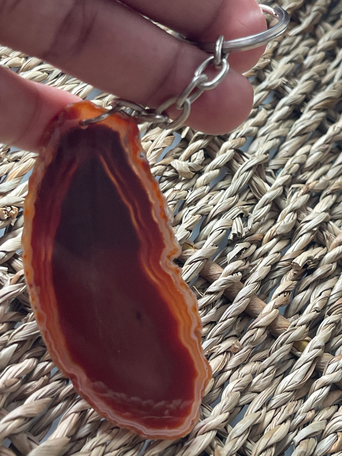 Agate stone keychain held by a hand on a woven mat background