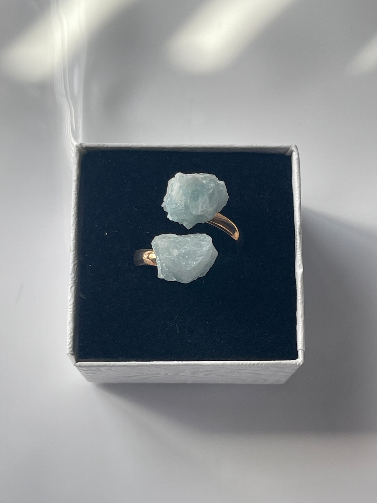 Pair of raw crystal Aquamarine Adjustable Natural Gold Ring on a dark black box with a white background