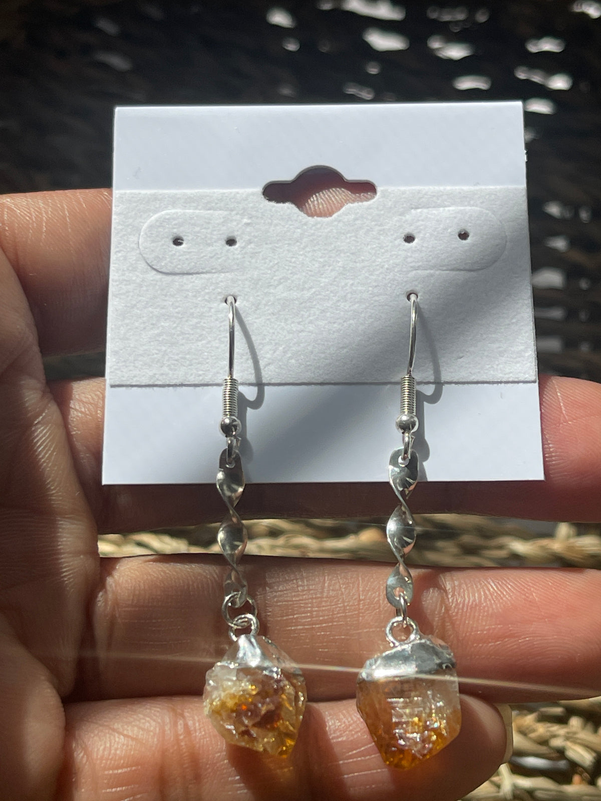 Citrine Crystal Point Spiral Earrings, Hand holding a pair of earrings with clear and amber stones on a white card.
