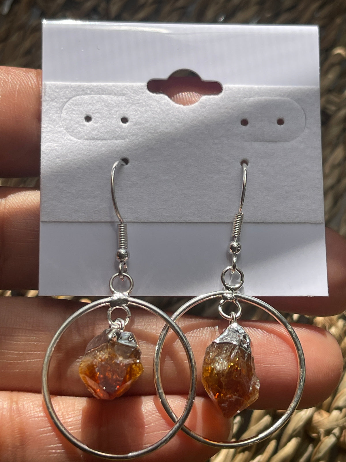 Citrine Point Circle Earrings, Silver hoop earrings with amber-colored stones held over a white card.