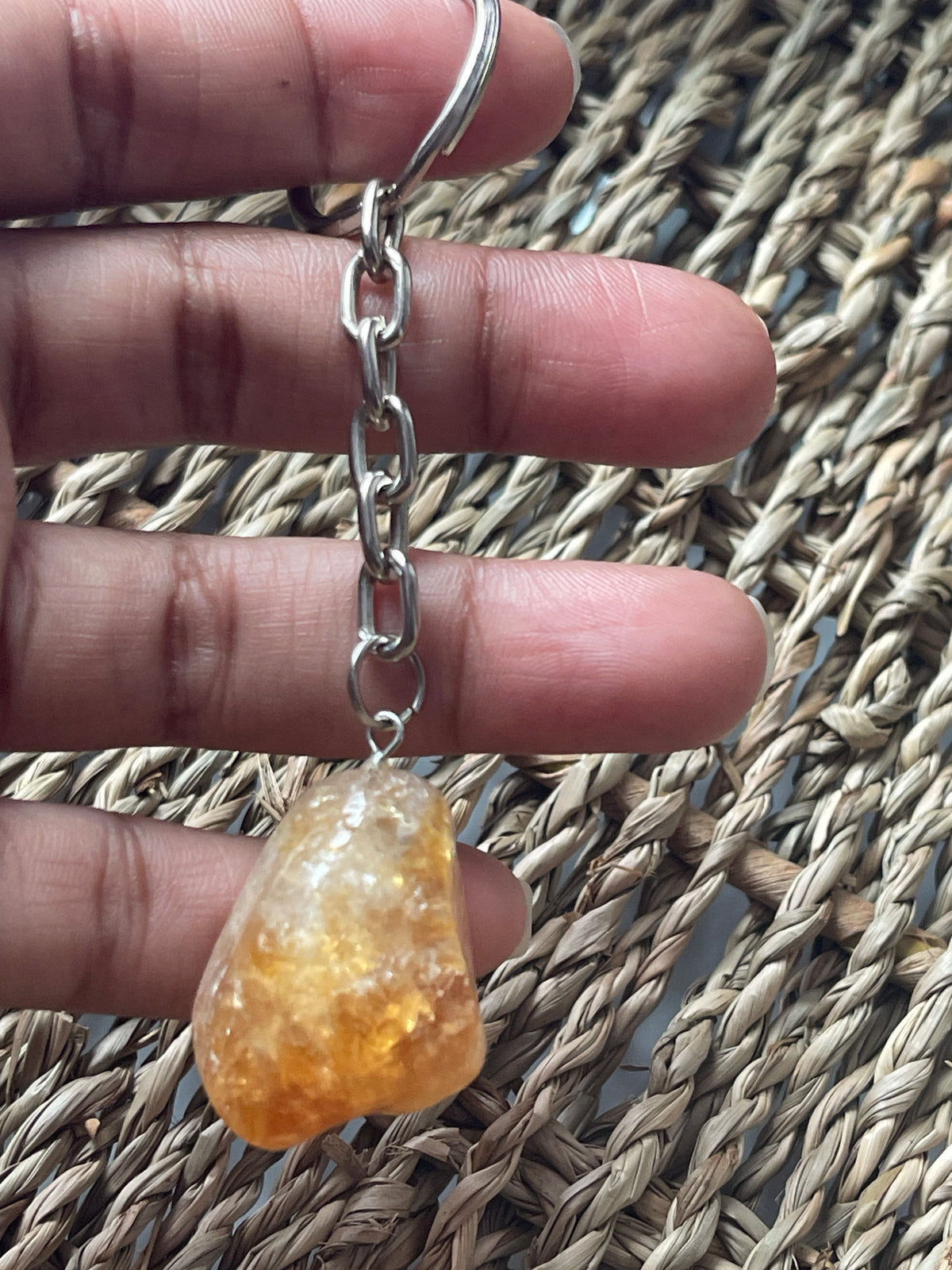 Hand holding a silver chain and a yellowish citrine stone against a woven background