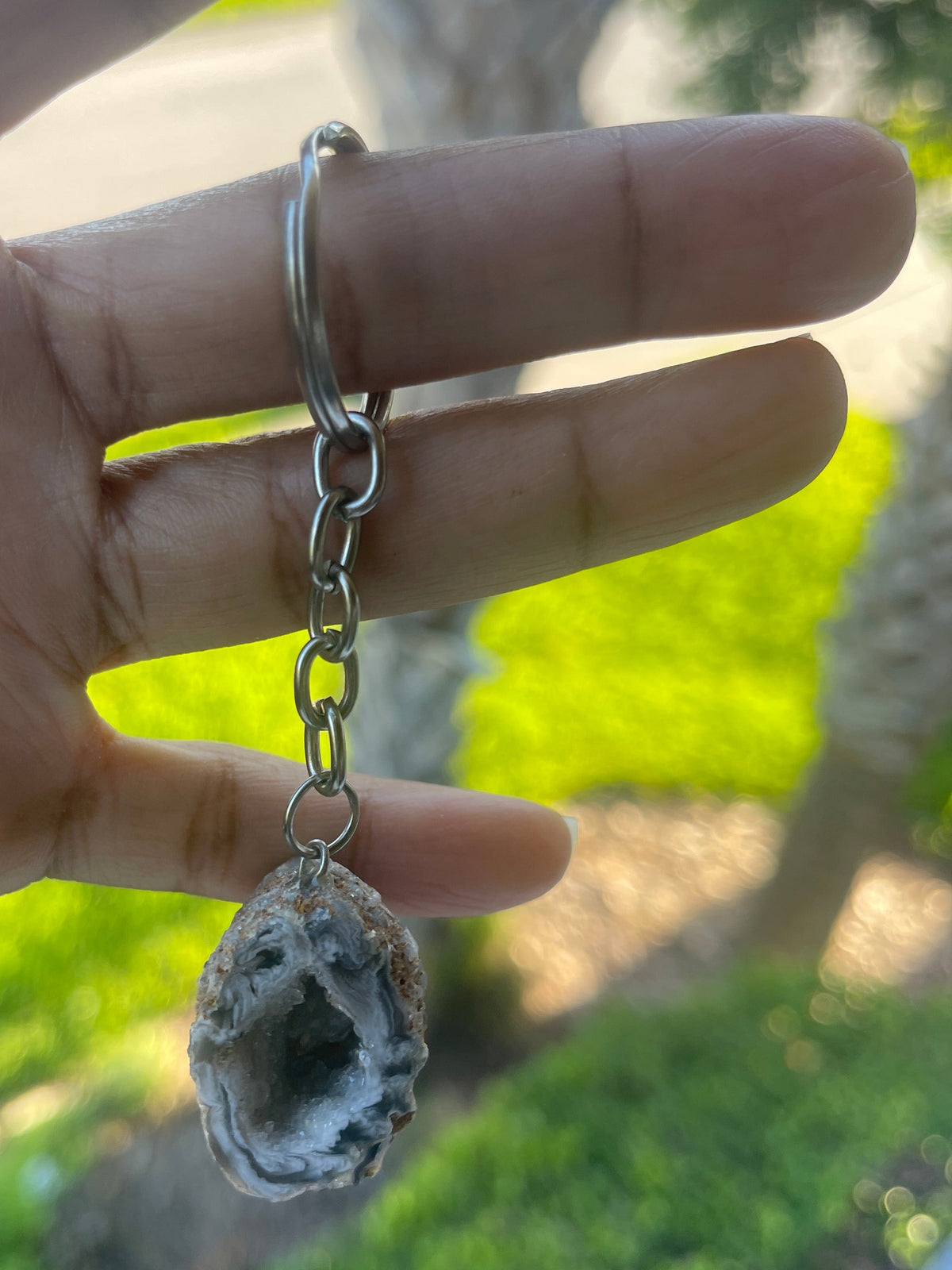 Hand holding a geode crystal on a chain with a natural outdoor background