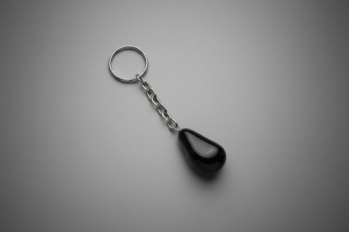 A polished black obsidian stone attached to a metal keychain ring, set against a gray background.