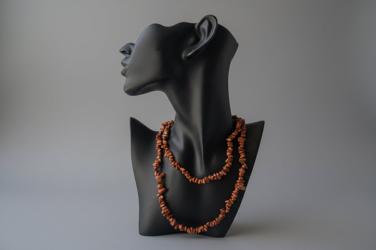 Red_Goldstone_Necklace_30-32_Inches on a black stand with a blurred in studio gray background