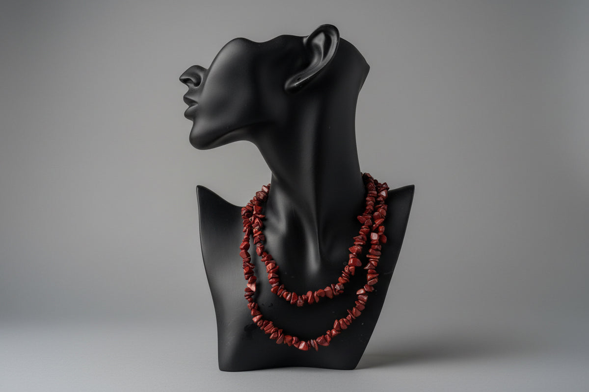 Black decorative necklace display object with Red_Jasper_Chip_Necklace_30-32_Inches red beads on a gray surface