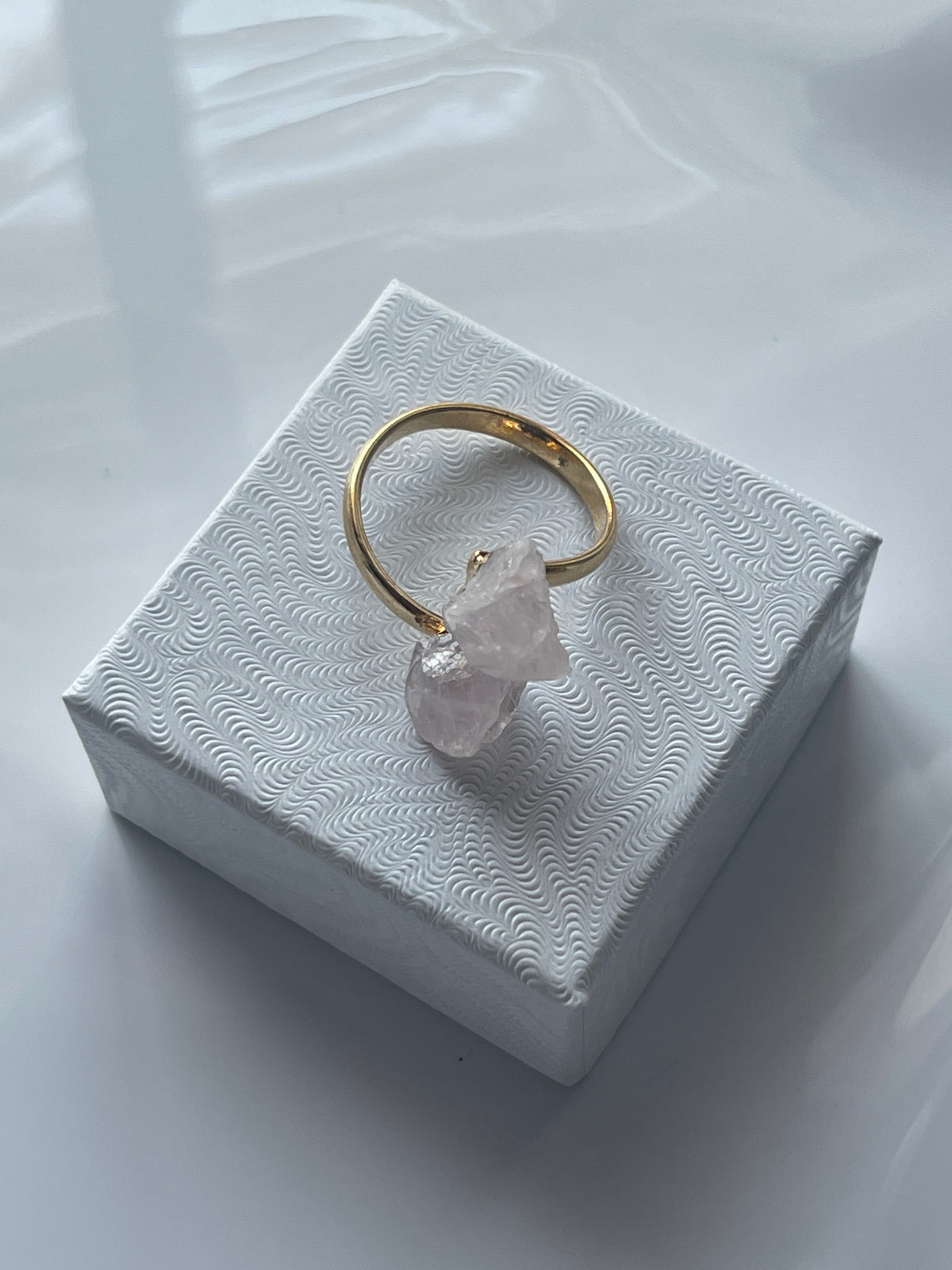 Rose quartz gold ring with a pink crystal on a textured white jewelry box