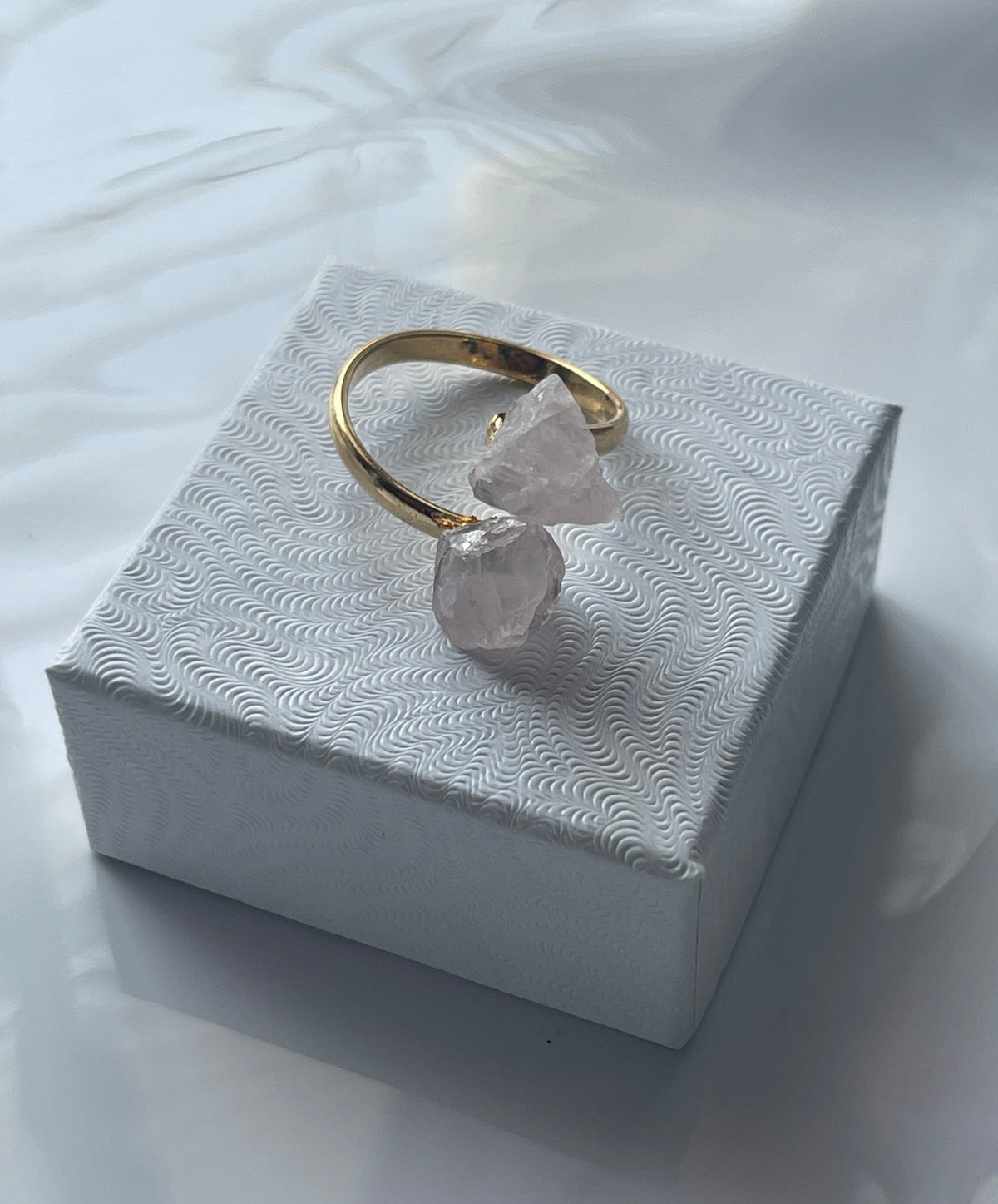 Rose quartz gold ring with a pink crystal on a textured white jewelry box top