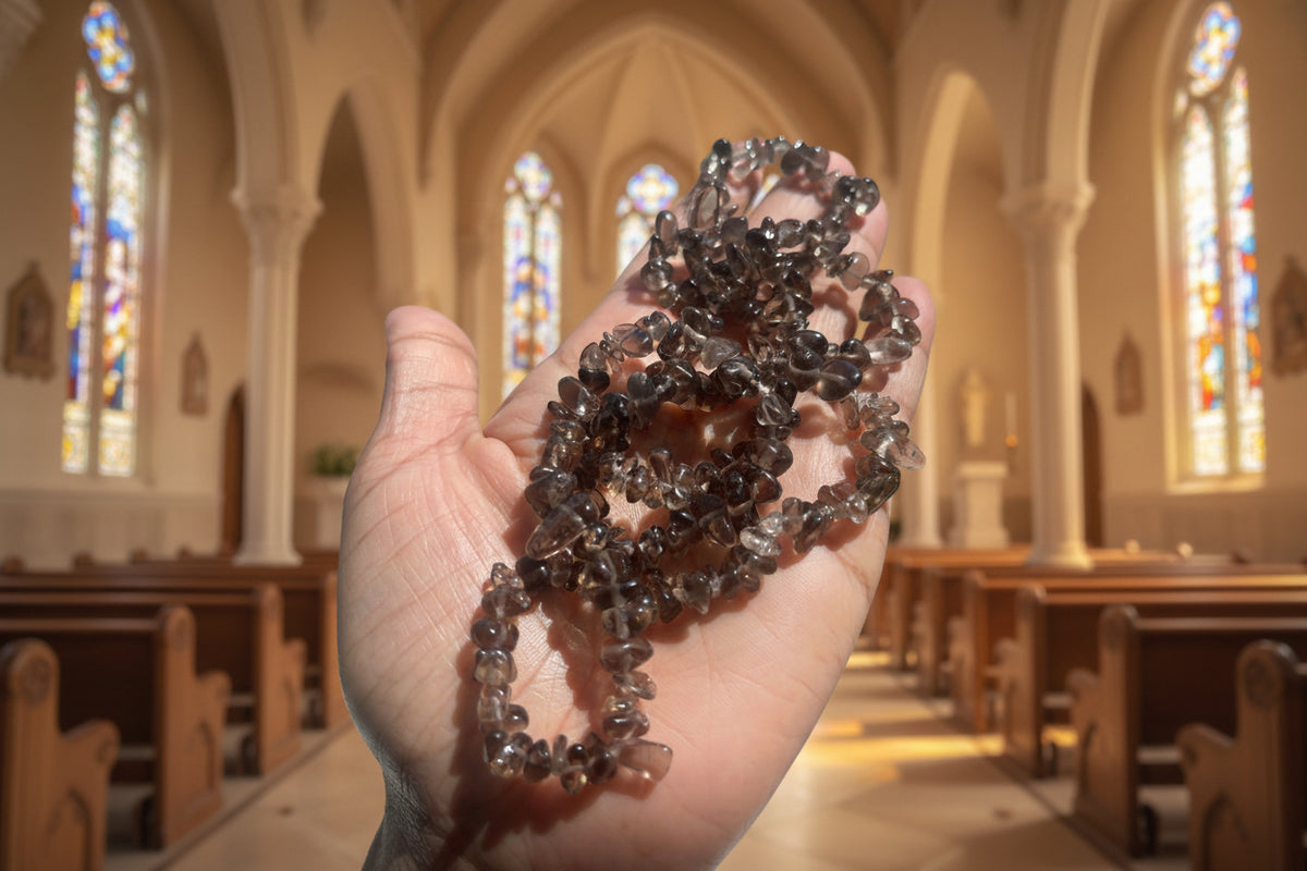 Hand holding smoky-quartz-necklaces-30-32-inches brown beads against a blurred chapel background