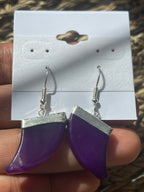 Purple and silver earring held by a hand with a blurred background