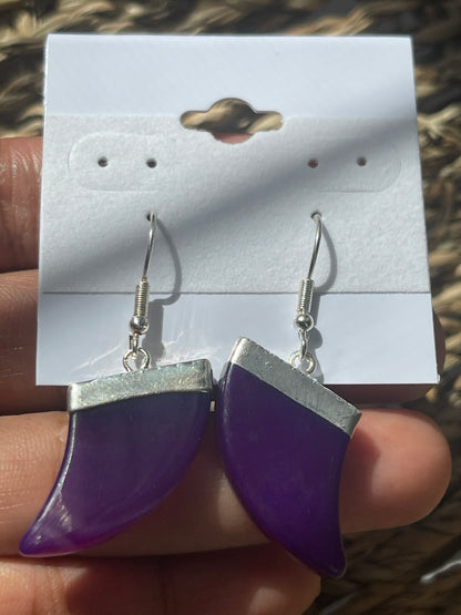 Purple and silver earring held by a hand with a blurred background