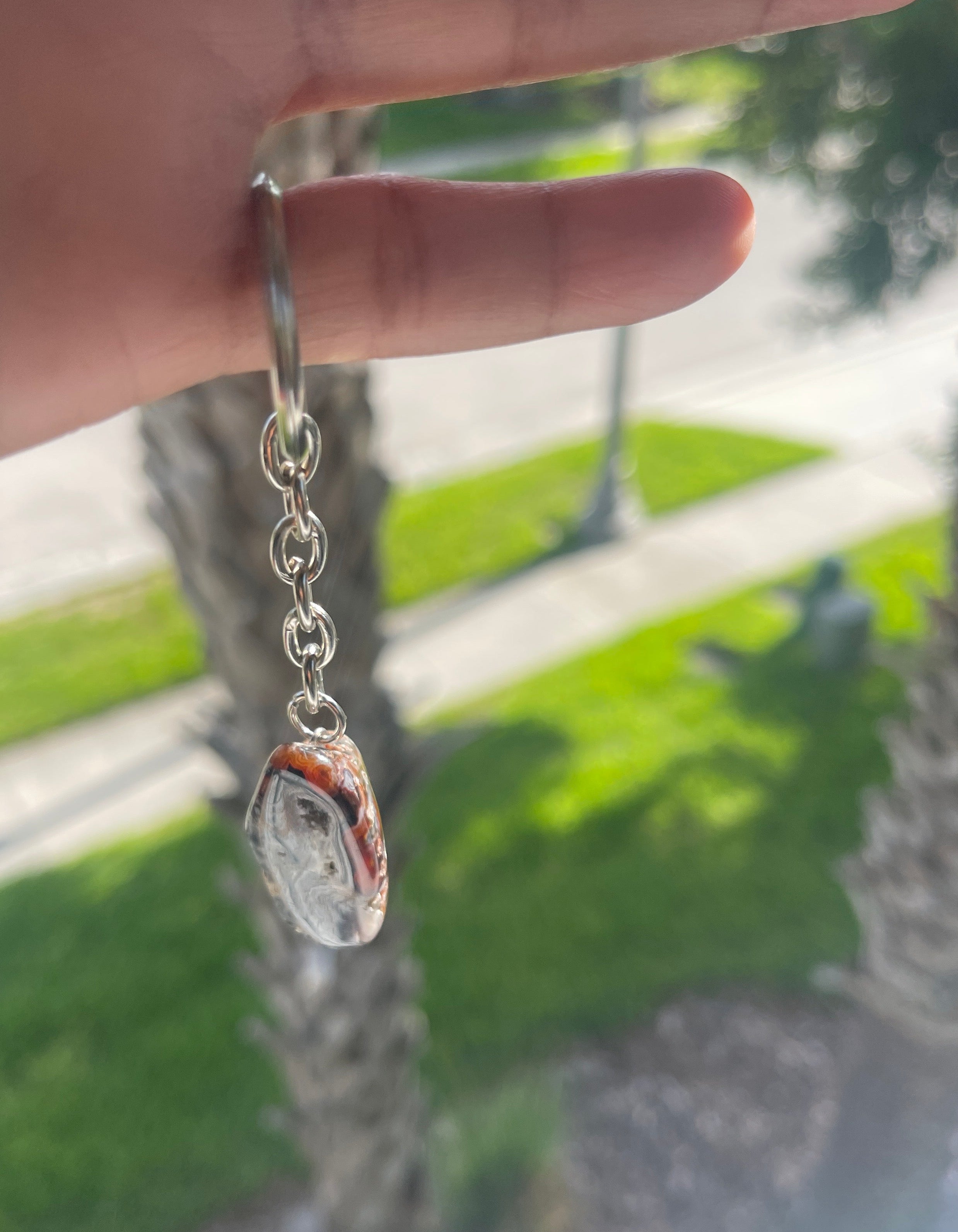 Hand holding a silver bracelet with a Agate Nodule Mix Keychain charm against a blurred green outdoor background