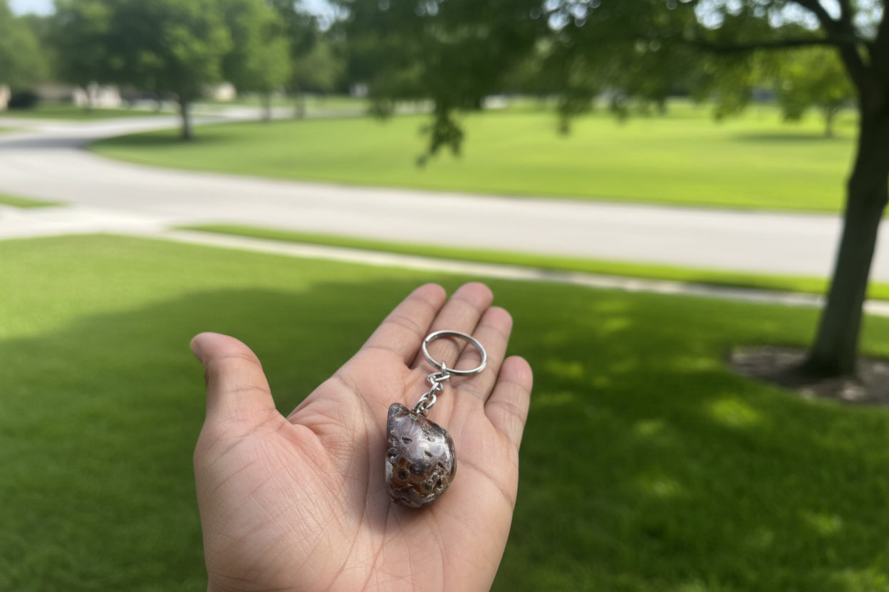 Hand holding a Agate Nodule Mix Keychain with a textured stone pendant against a blurred outdoor background