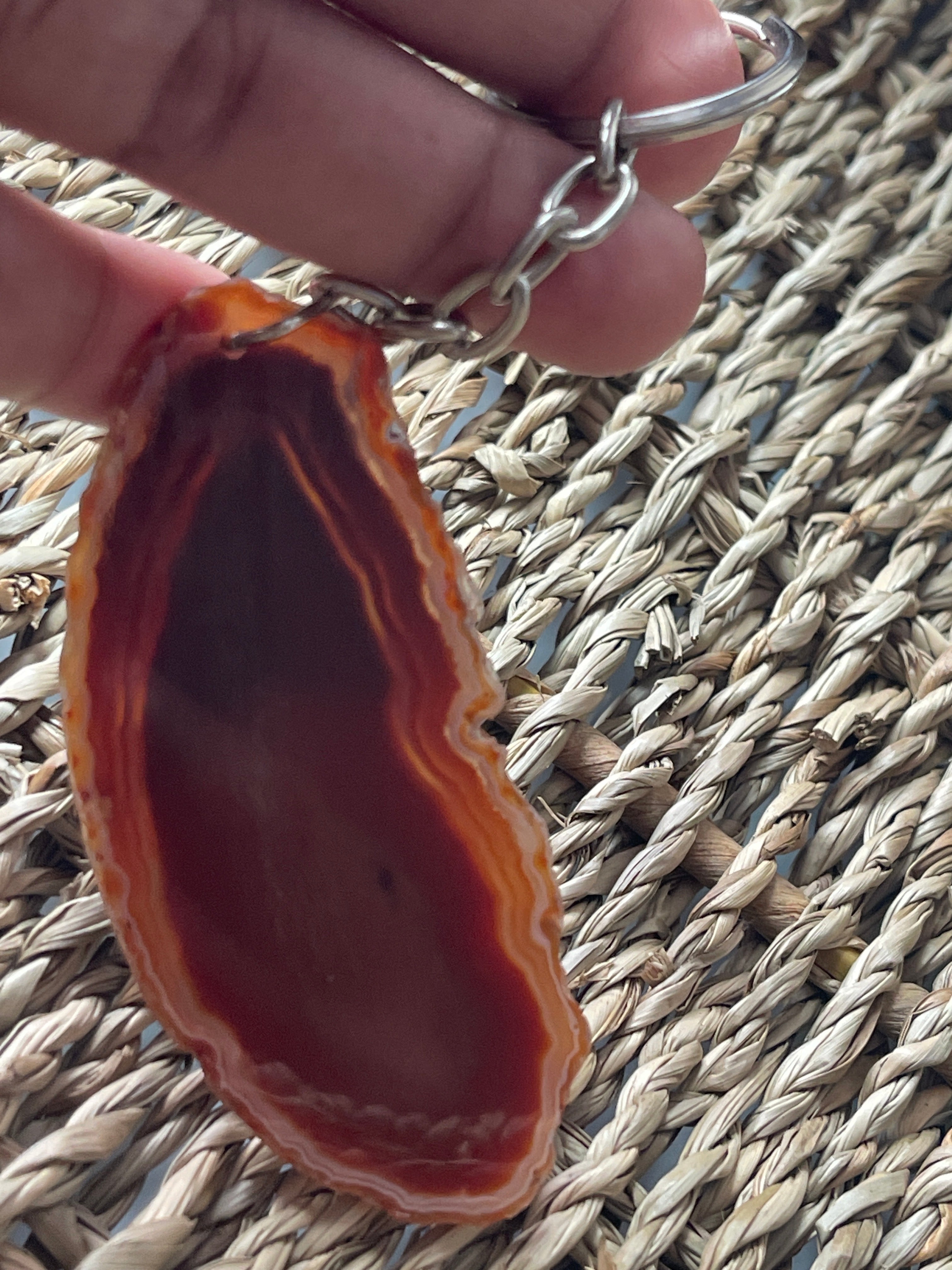 Agate stone keychain held by a hand on a woven mat background