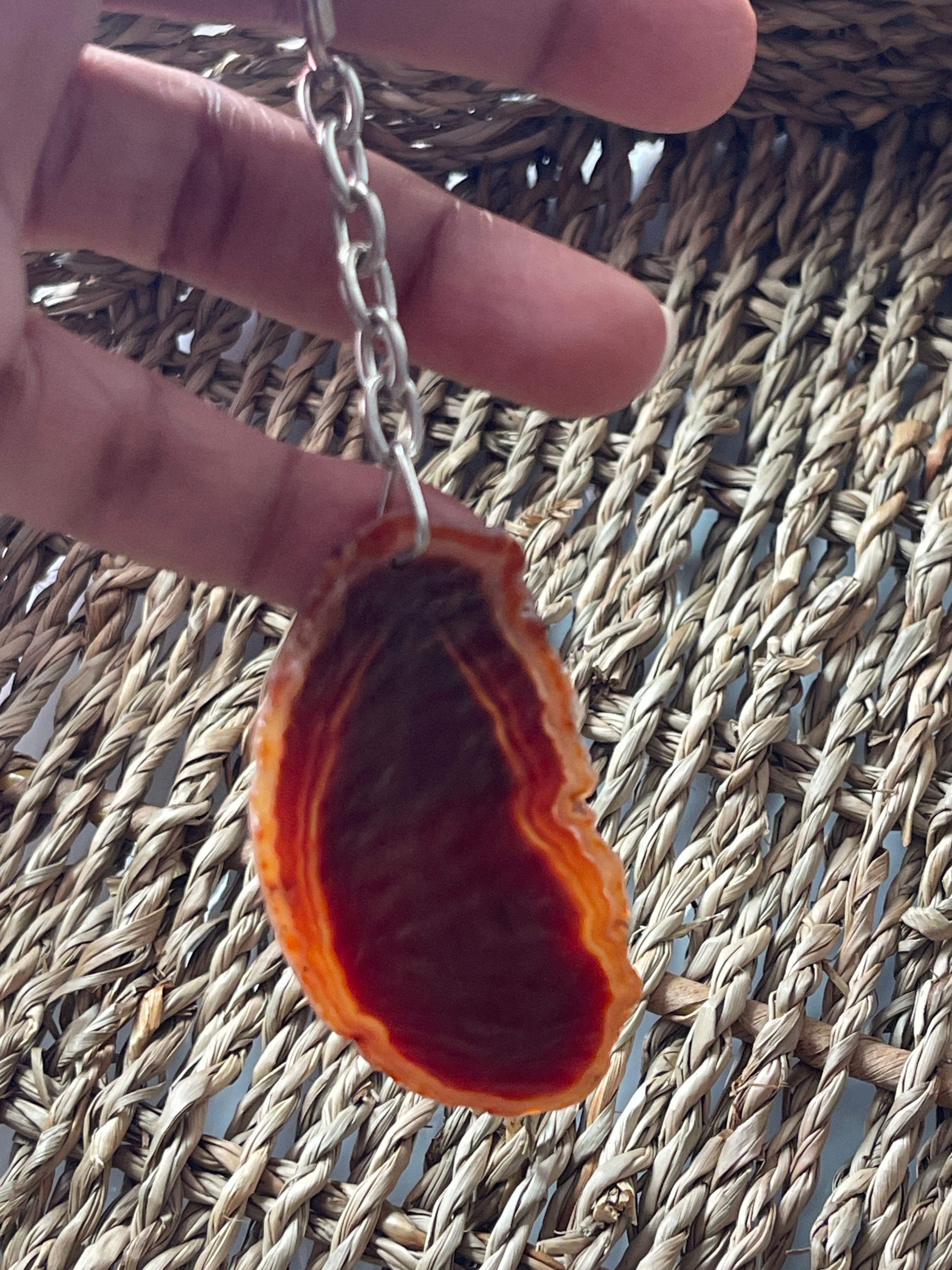 Hand holding a split open red and brown Agate slice Keychain with a chain against a woven mat background