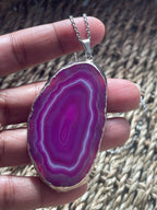 Agate pendant with purple interior held between fingers against a textured background