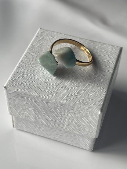 Close-up of a textured white surface with a gold plated Amazonite ring and green stone on a light gray background