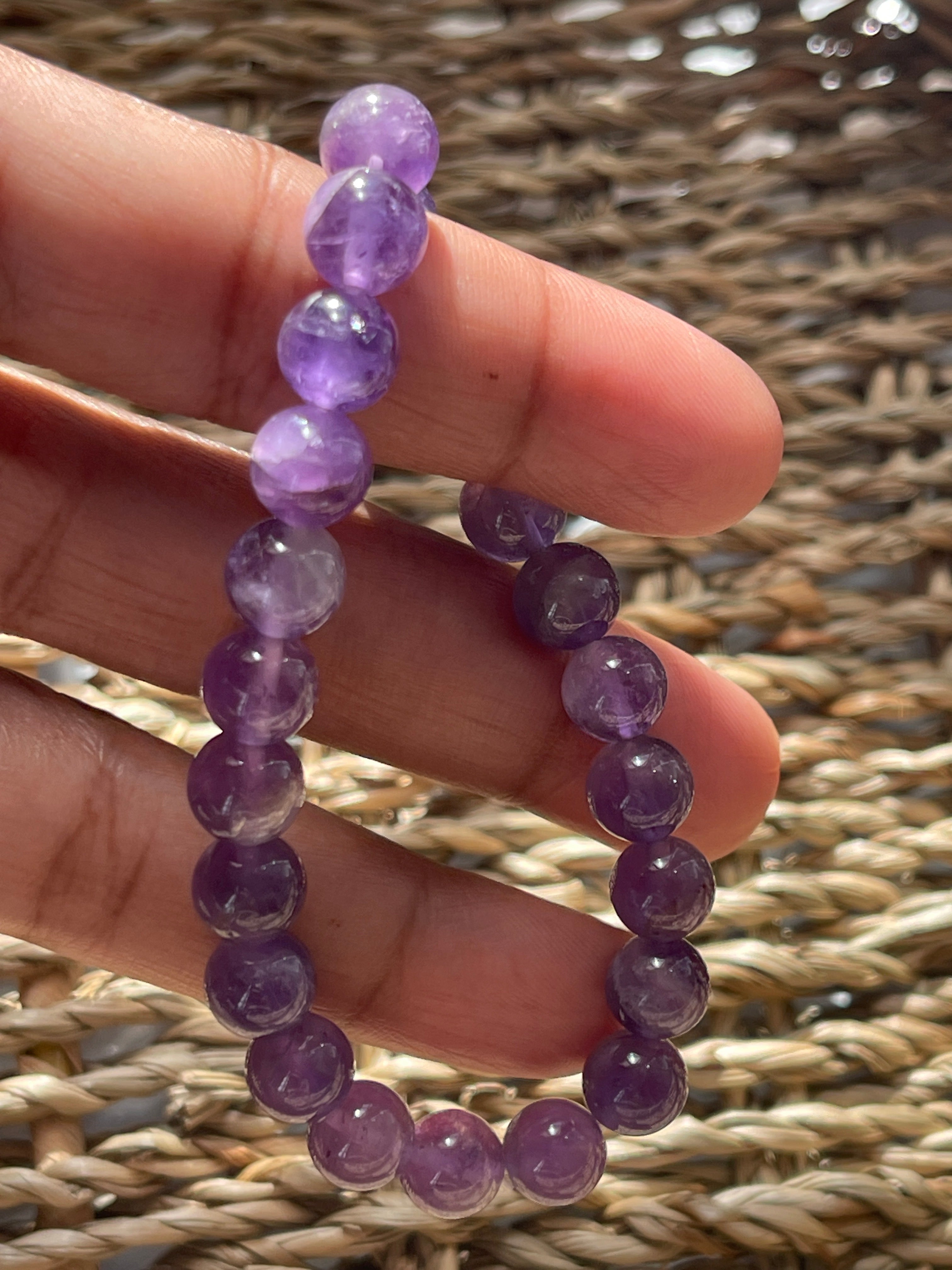 Purple beaded bracelet held in a hand against a woven background