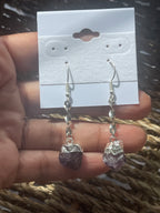 Amethyst Crystal Point Spiral Earrings with purple stones held over a display card on a textured surface