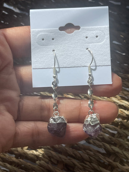 Amethyst Crystal Point Spiral Earrings with purple stones held over a display card on a textured surface