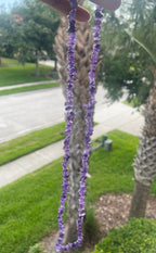 Purple beaded Amethyst_HQ_Necklace held up to a palm tree with a blurred background