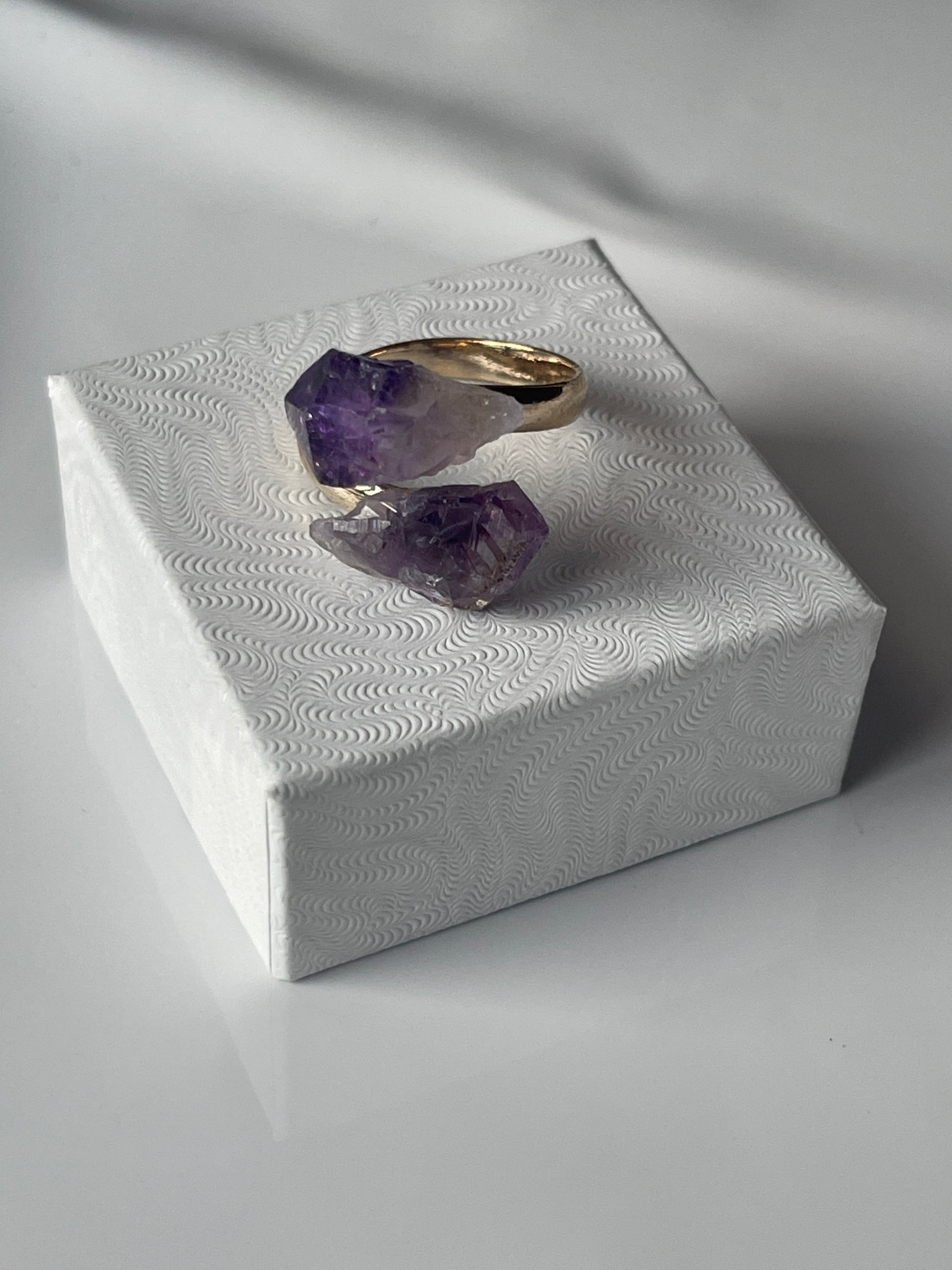 Amethyst ring on a textured white stand with soft lighting