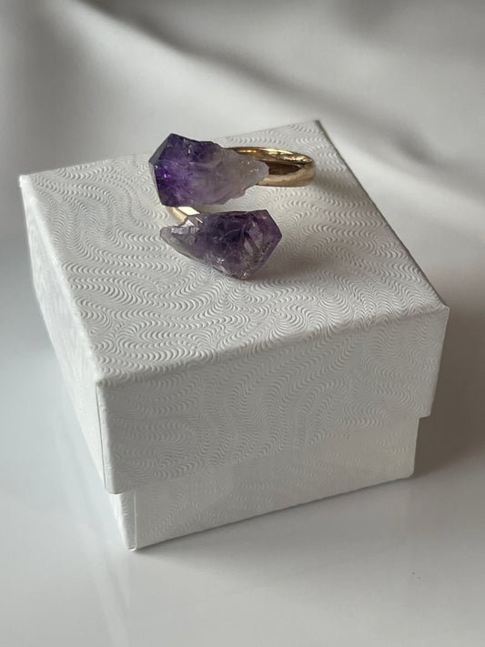 Amethyst crystal on a gold stand with a white textured box in the background