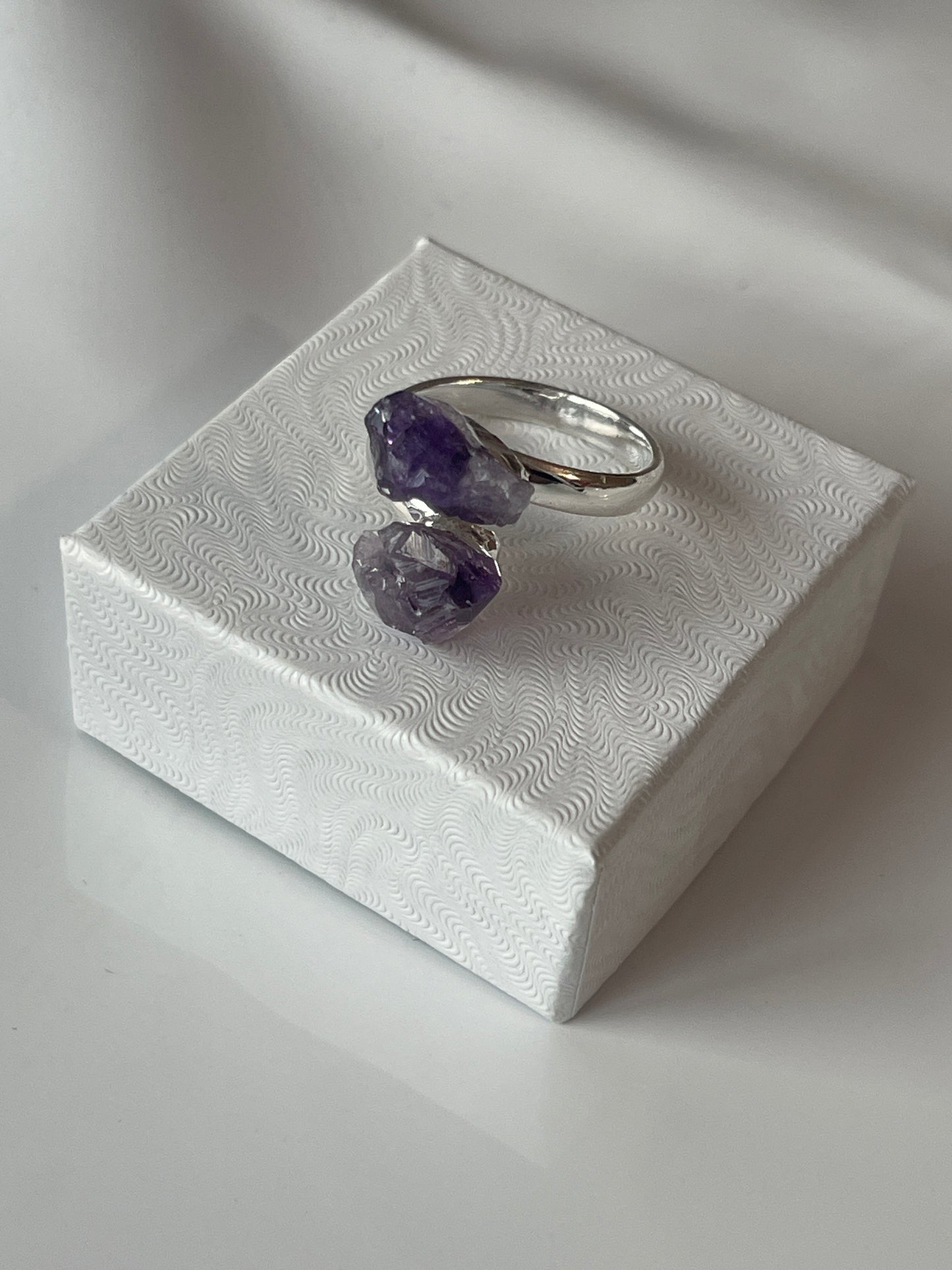 Silver ring with purple gemstones on a textured white surface