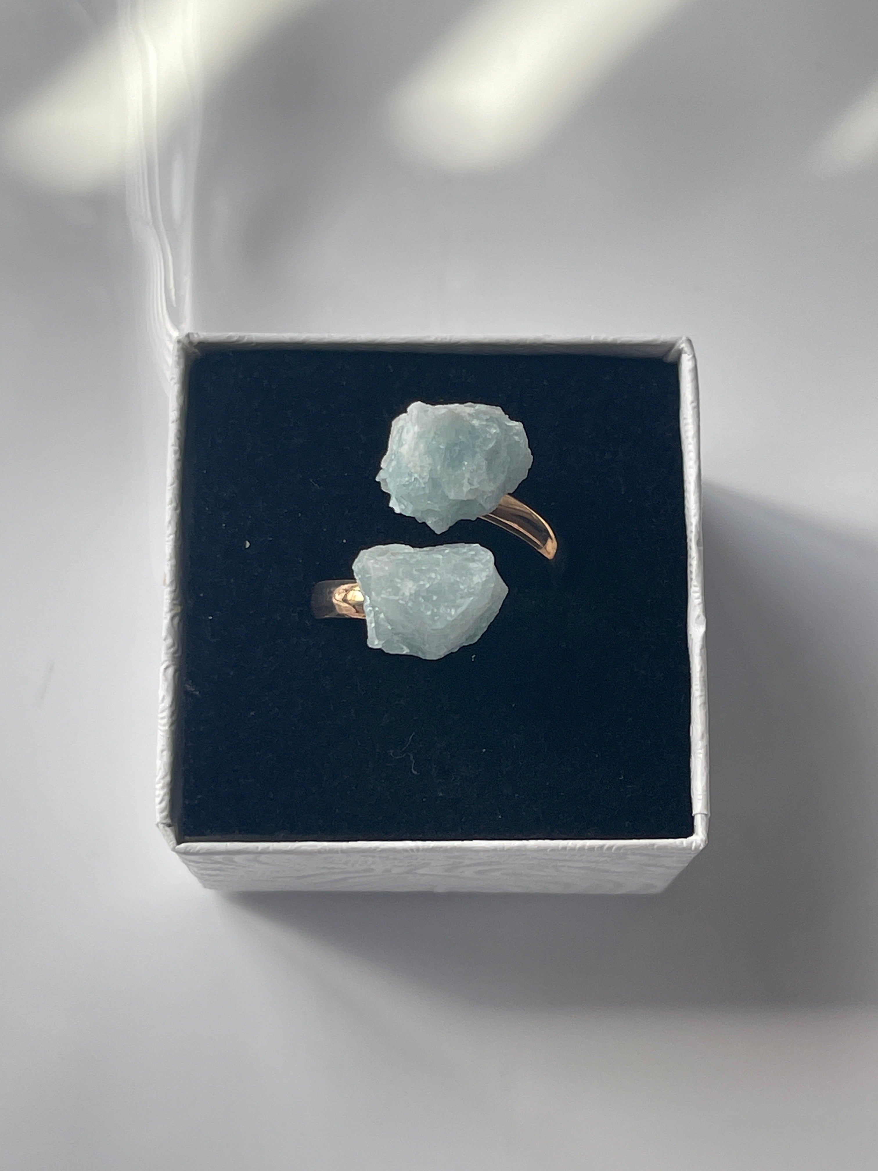 Pair of raw crystal Aquamarine Adjustable Natural Gold Ring on a dark black box with a white background