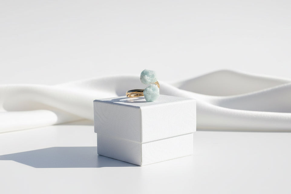 Gold ring with green gemstones known as Aquamarine Adjustable Natural Gold Ring on a textured white jewelry box