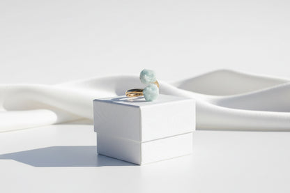 Gold ring with green gemstones known as Aquamarine Adjustable Natural Gold Ring on a textured white jewelry box