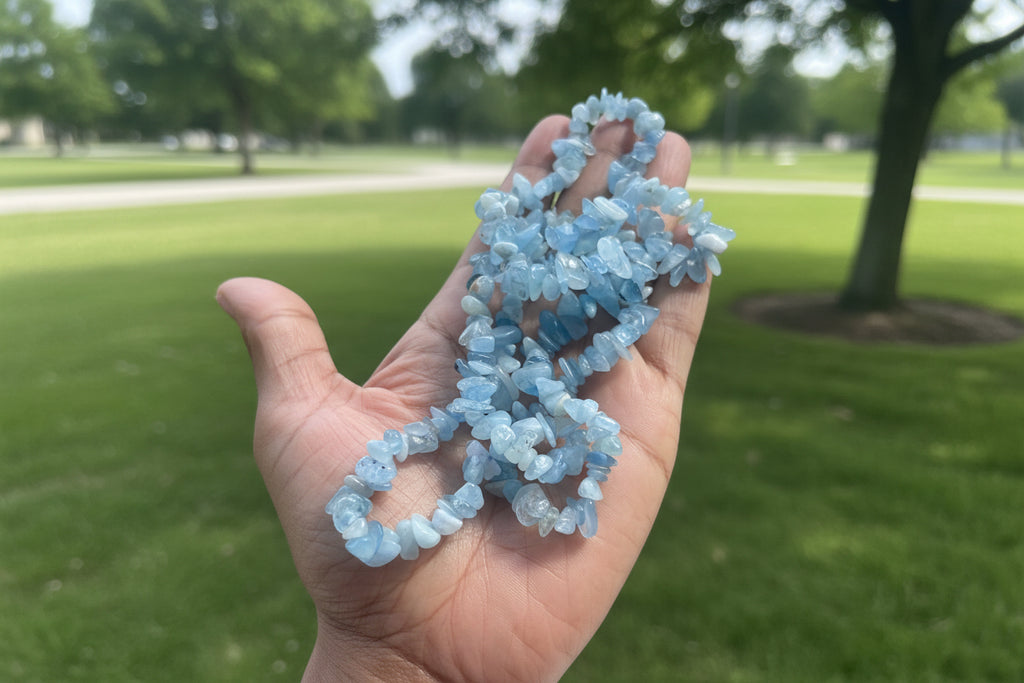 Hand holding a Aquamarine Necklace of blue crystal beads with a blurred park background