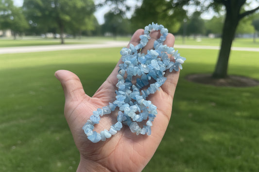 Hand holding a Aquamarine Necklace of blue crystal beads with a blurred park background