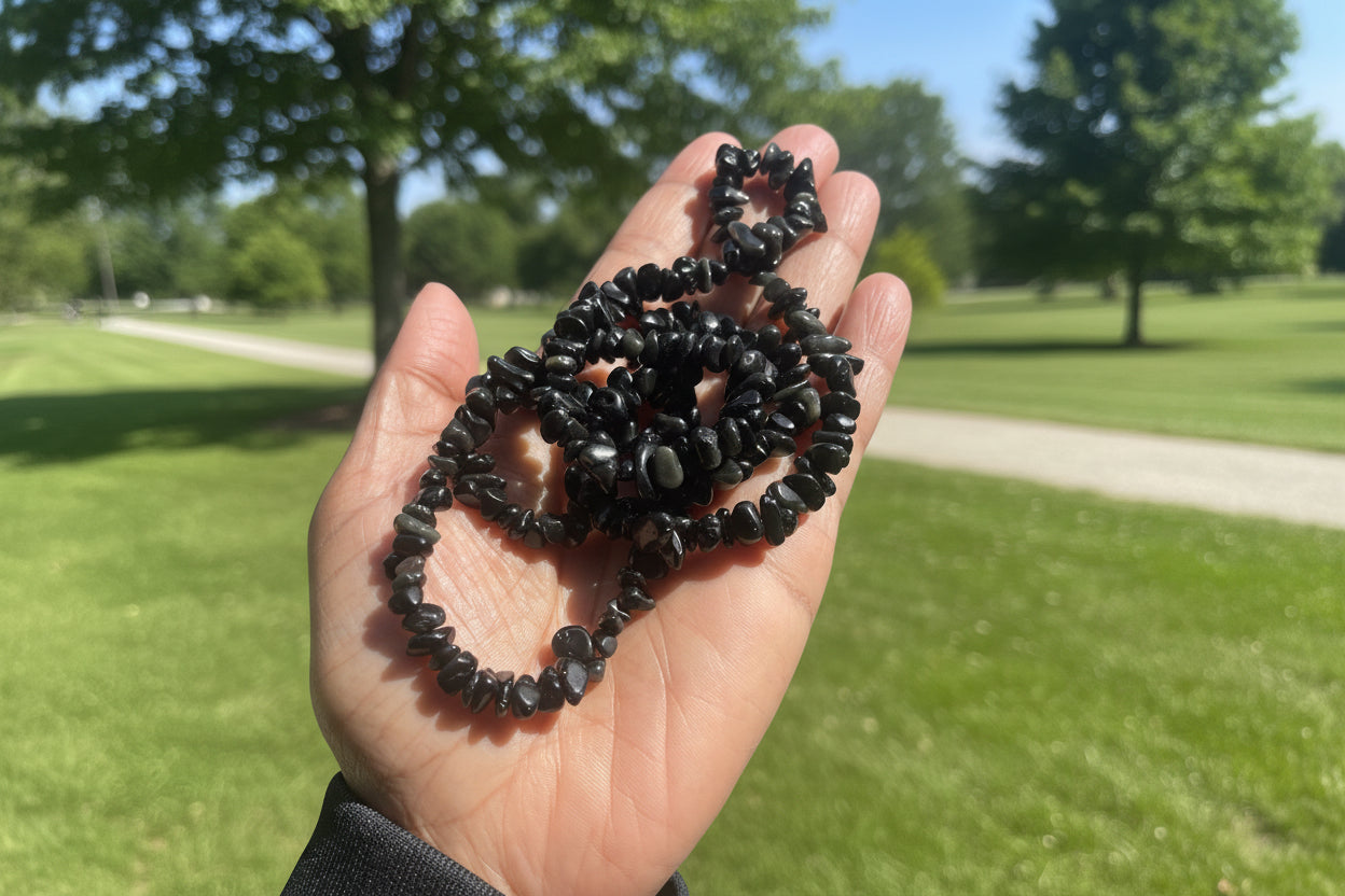 Hand holding a coiled black stone Obsidian Chip Necklace against a blurred park background