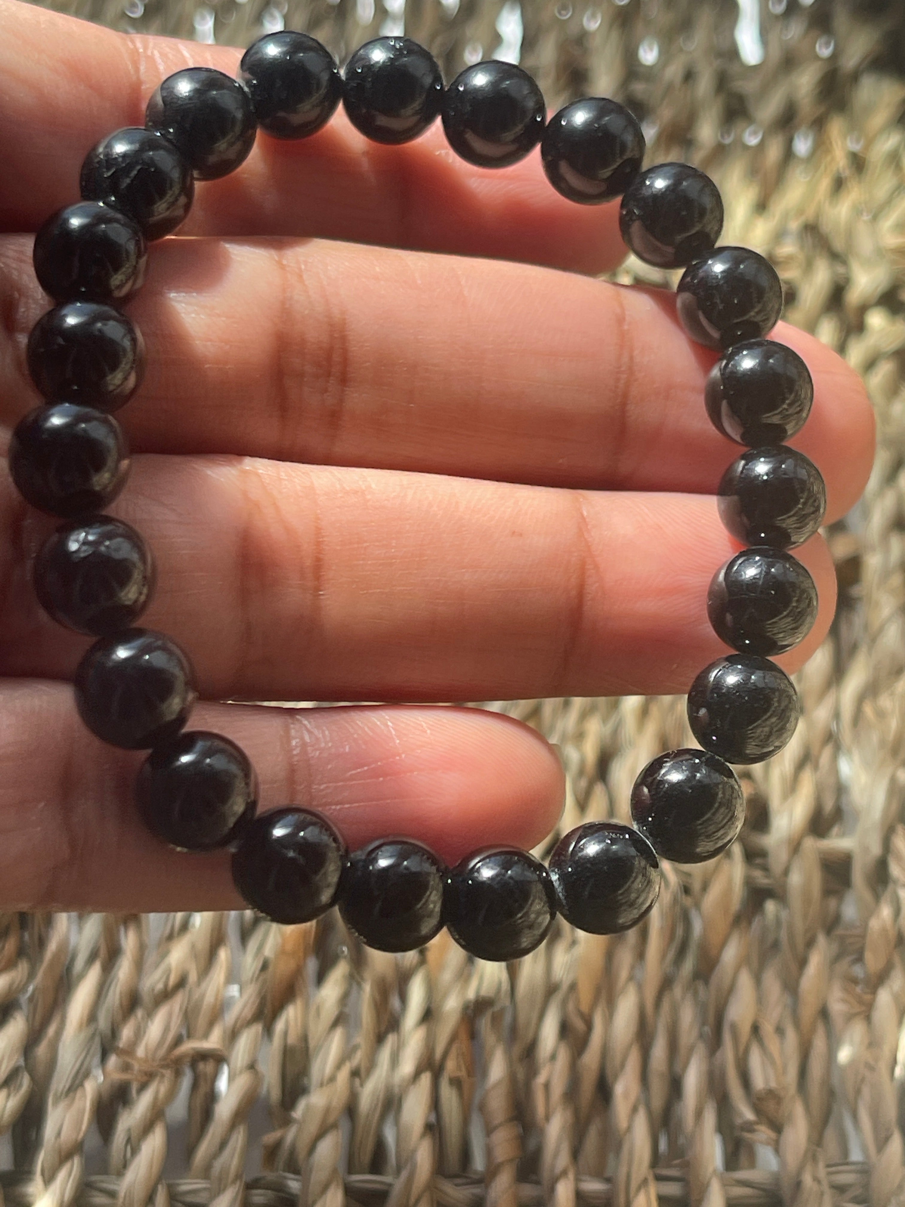 Black beaded bracelet on a hand with a woven background