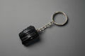 A natural black tourmaline chunk attached to a silver-colored keychain base, set against a gray background.