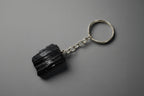 A natural black tourmaline chunk attached to a silver-colored keychain base, set against a gray background.