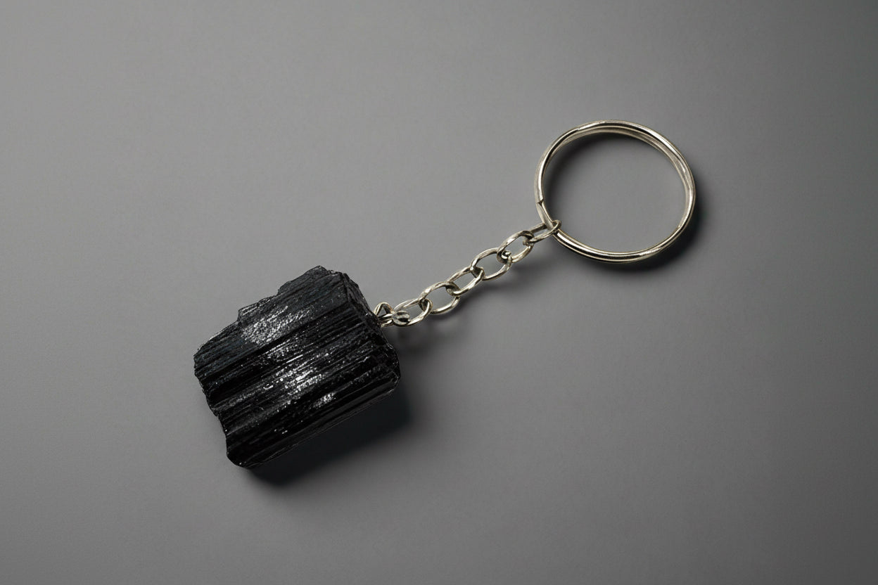 A natural black tourmaline chunk attached to a silver-colored keychain base, set against a gray background.