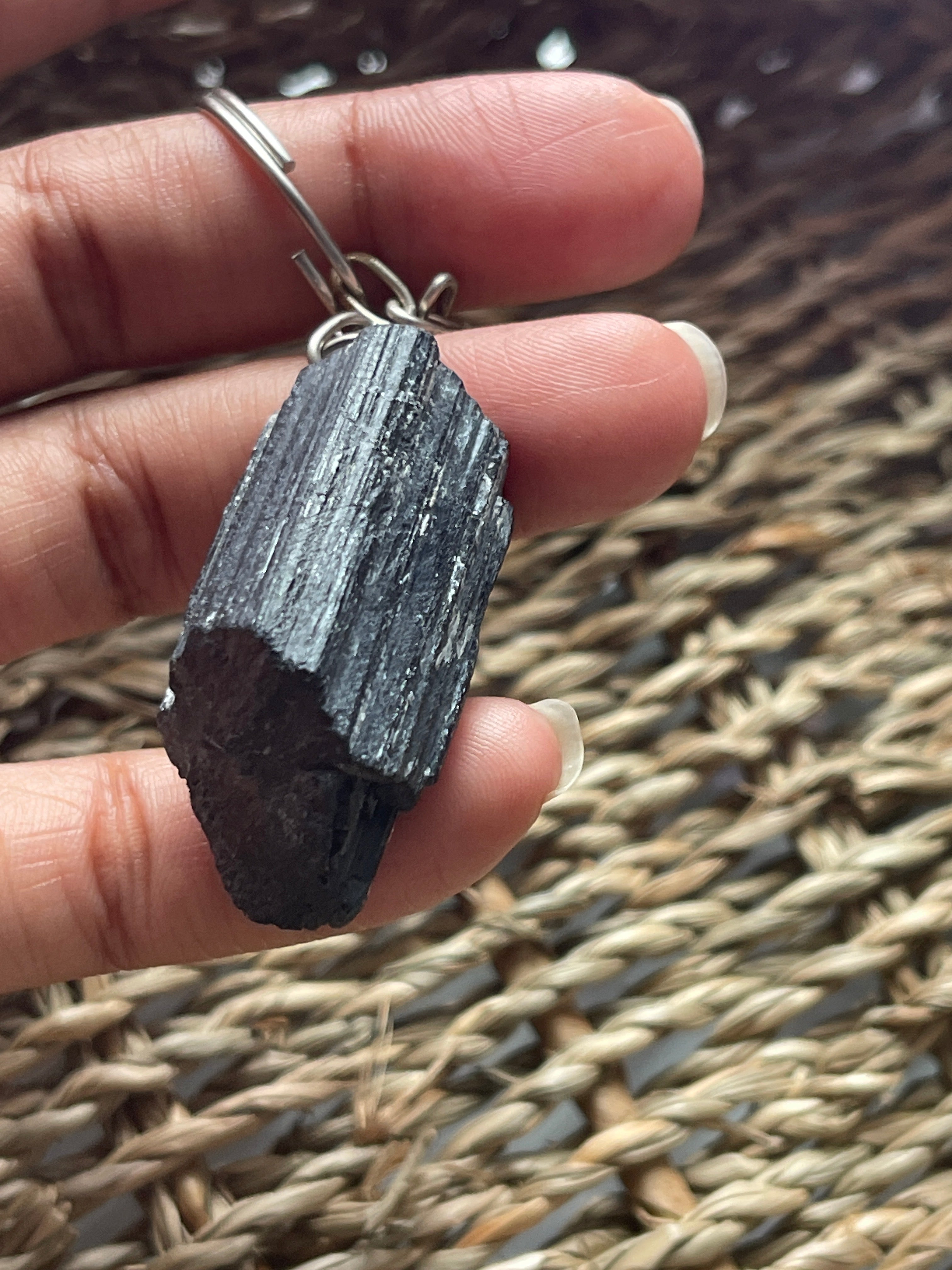 Black Tourmaline Keychain in Hand holding a dark stone with a woven mat background