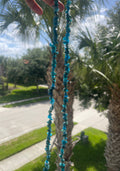 Blue beaded necklace held up to a palm tree with a road and buildings in the background