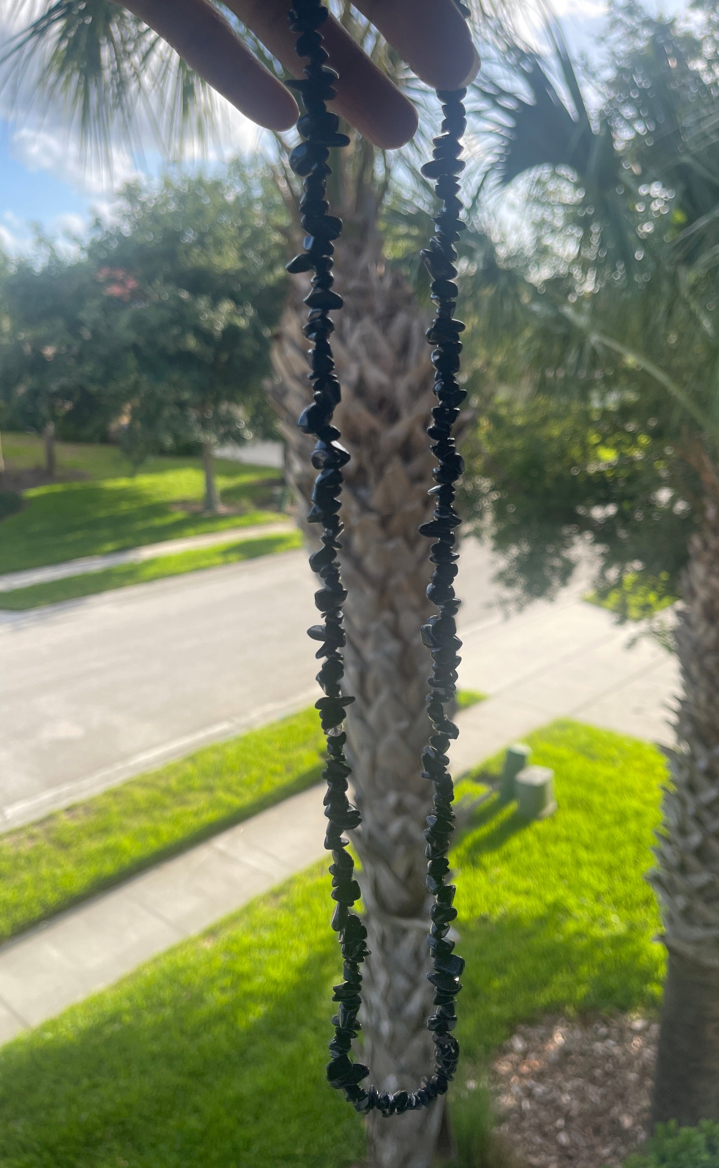 Blue beaded Blue_Goldstone_Necklace_30-32_Inches held up with a blurred outdoor background