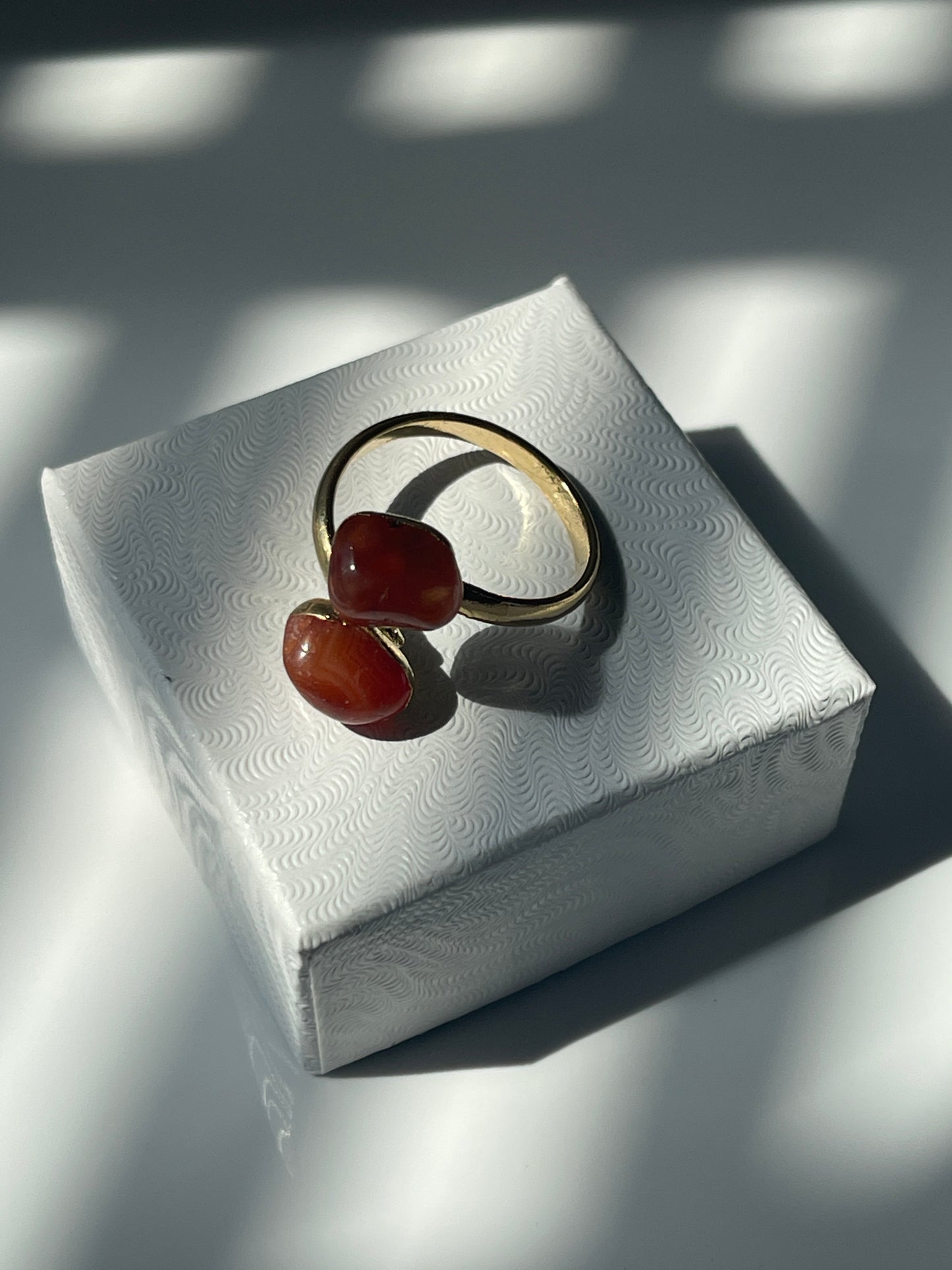 Carnelian Agate gold plated ring with orange stones on a textured white jewelry box top 