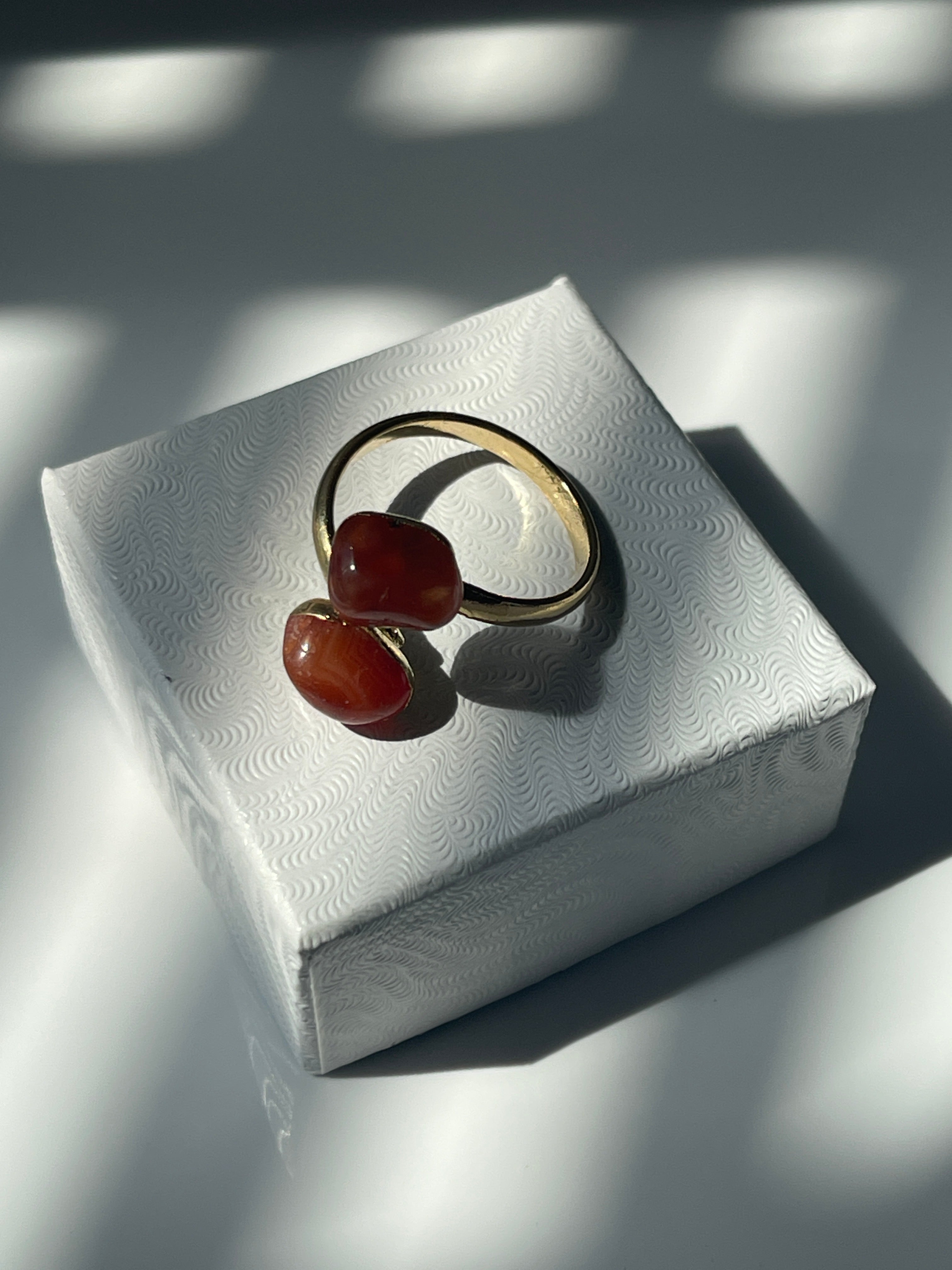 Carnelian Agate gold plated ring with orange stones on a textured white jewelry box top 
