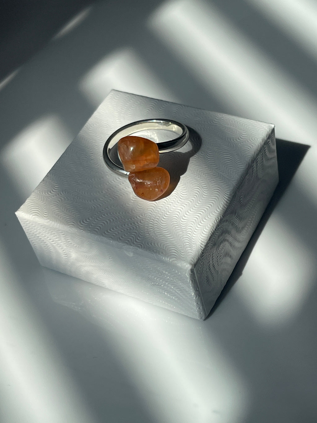 Carnelian Agate adjustable silver plated ring sitting on top of a white small jewelry box top in the sunlight 