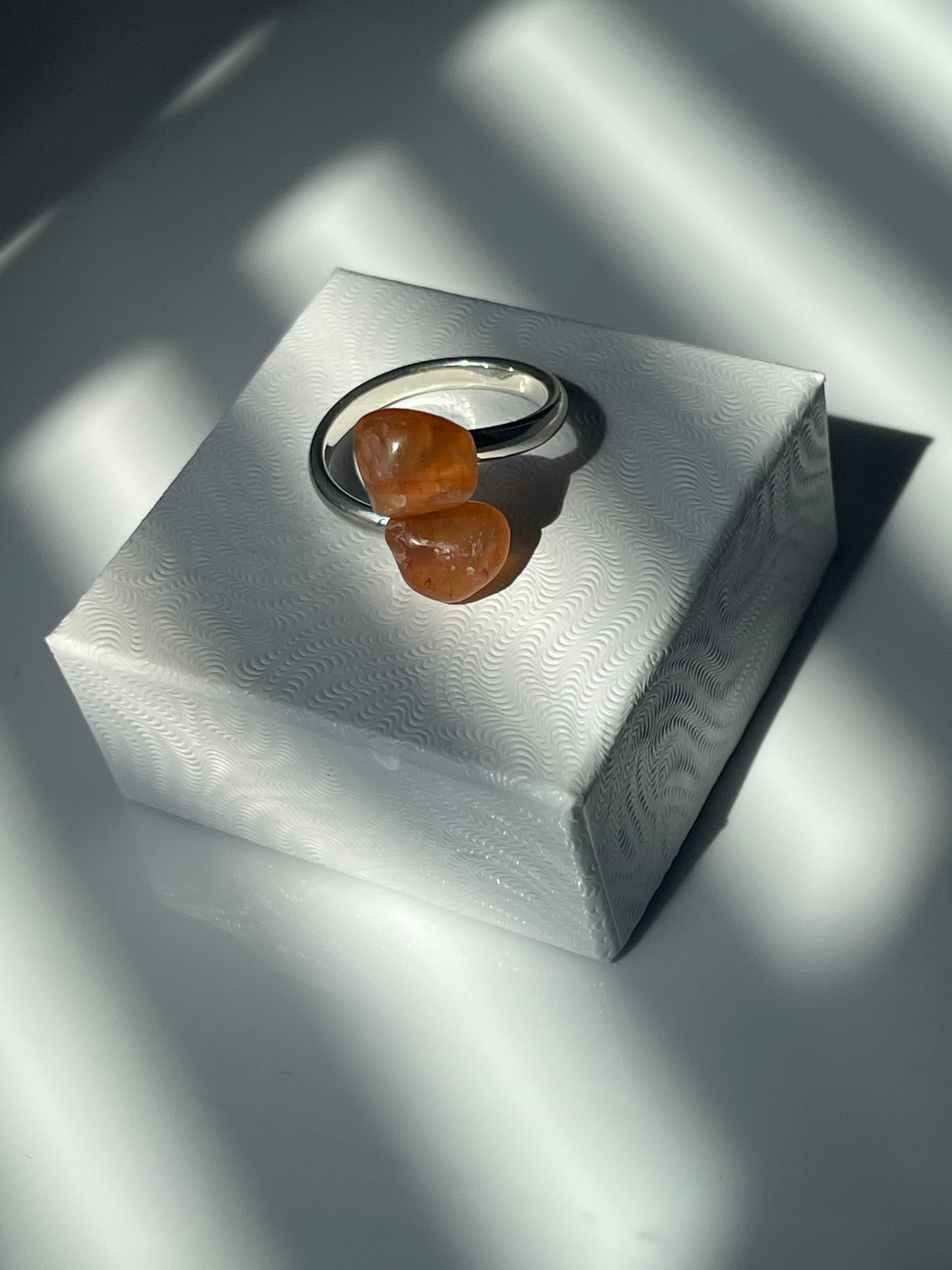 Carnelian Agate adjustable silver plated ring sitting on top of a white small jewelry box top in the sunlight 