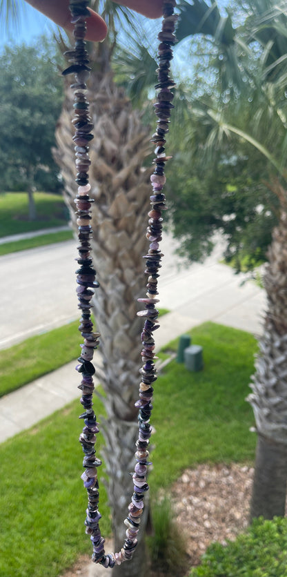 Close-up of a beaded Charoite_Necklace_30-32_Inches held against a palm tree background