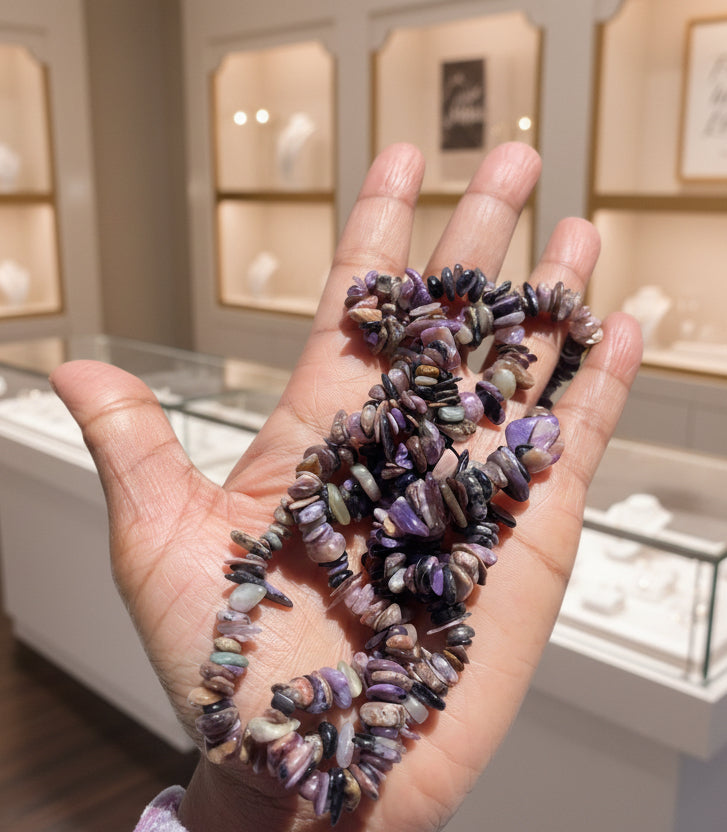 Hand holding a string of multicolored Charoite_Necklace_30-32_Inches beads against a blurred natural background