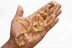 Hand holding a Citrine_Chip_Necklace_30-32_Inches light-colored beads with a white background