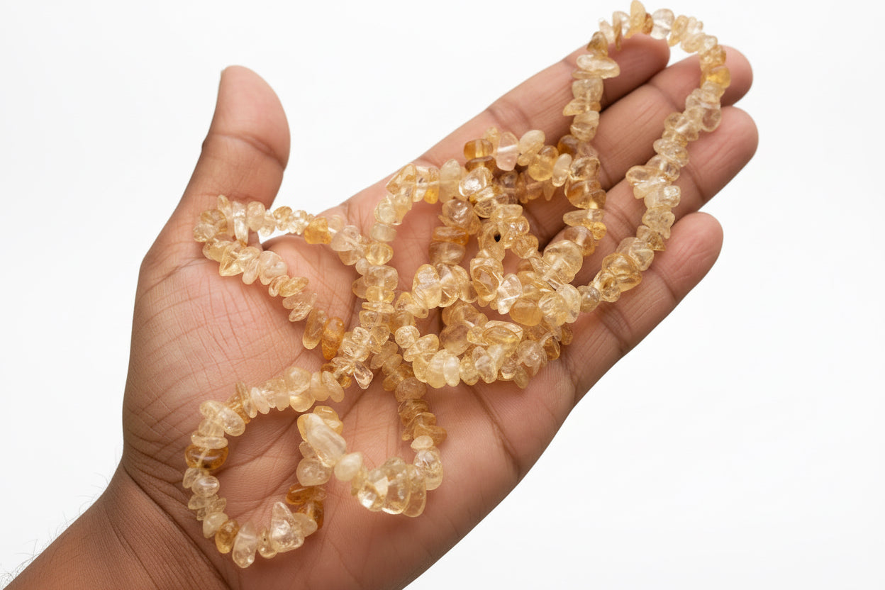 Hand holding a Citrine_Chip_Necklace_30-32_Inches light-colored beads with a white background
