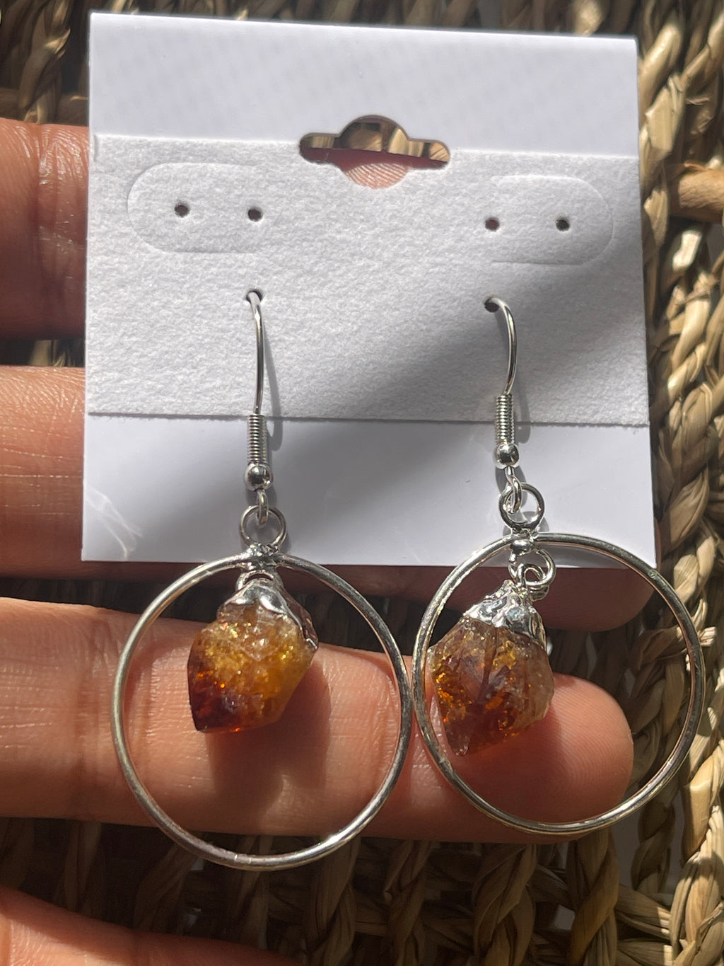 Citrine Point Circle Earrings, Round earrings with amber-colored crystals on a white card held by a hand.