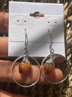 Citrine Point Circle Earrings, Round earrings with amber-colored crystals on a white card held by a hand.